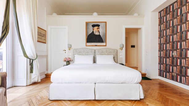 A large bed with a headboard, a wooden herringbone floor, a portrait above the bed, and a bookshelf to the right. - Relais Donna Lucrezia (Rome)