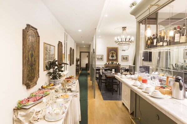 A hotel dining area with a buffet setup, a chandelier, and a wine display. - Relais Donna Lucrezia (Rome)