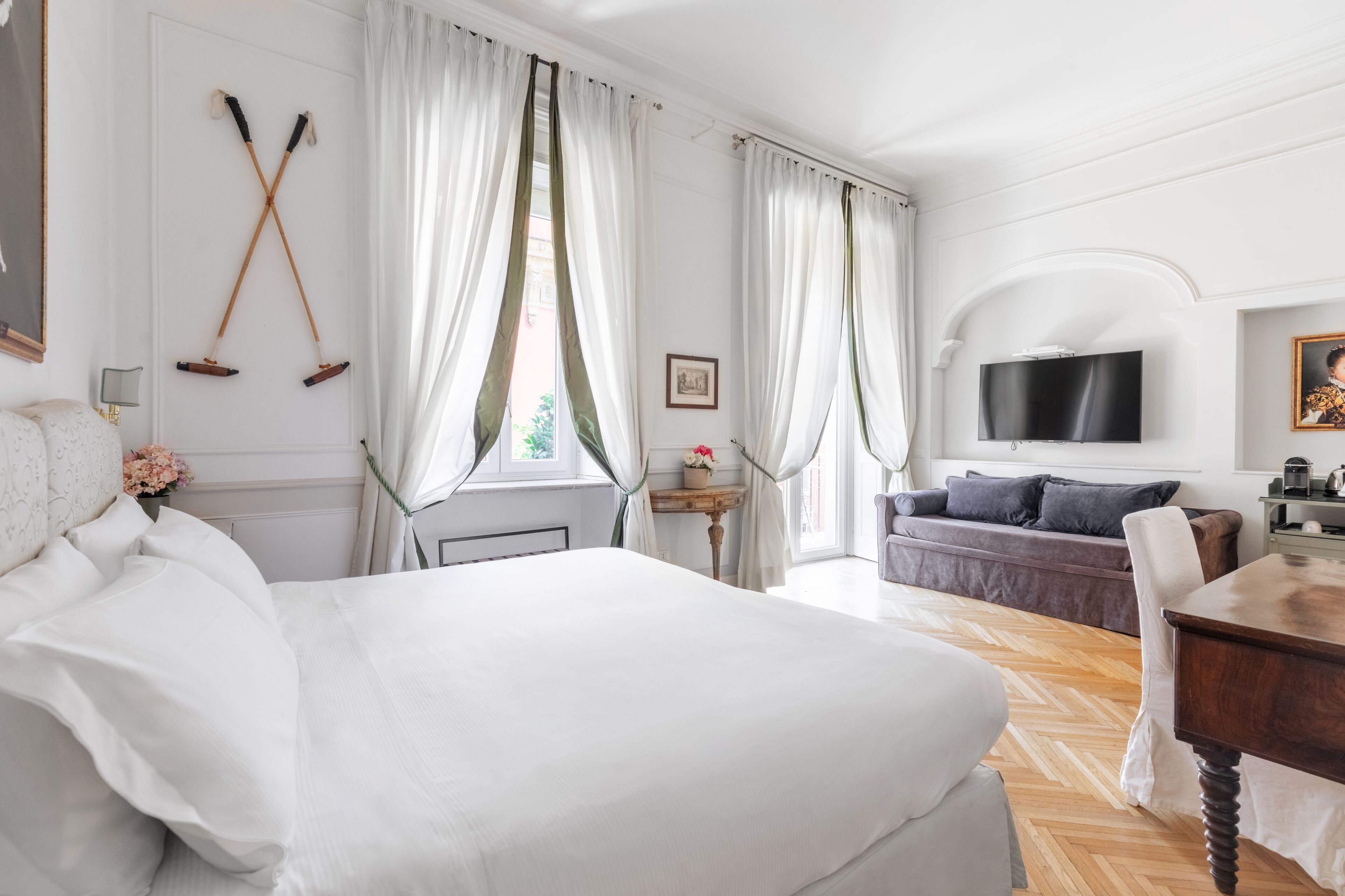 A hotel room with a large bed, a sofa, a TV, and a dining table.