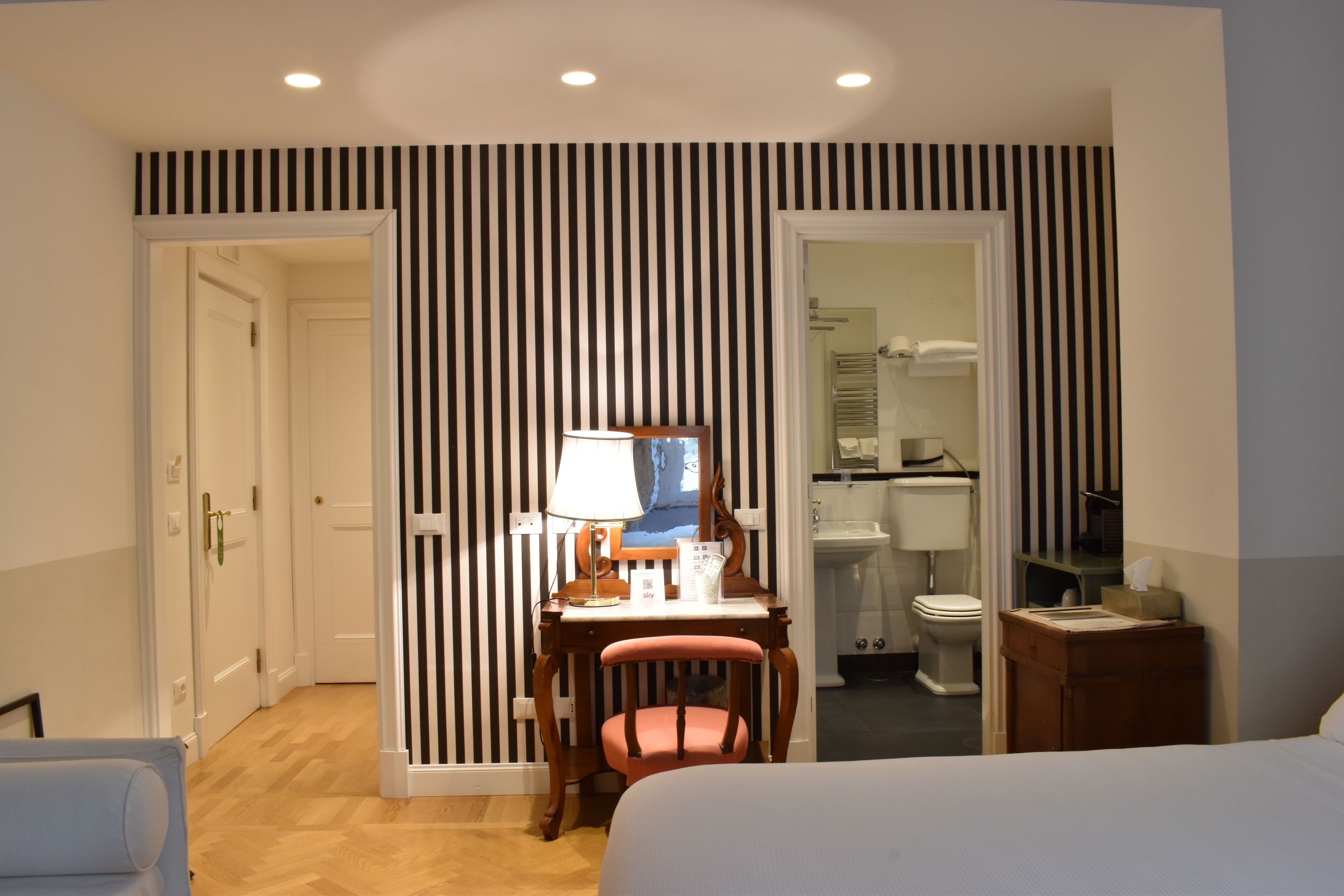 A hotel room with a bed, a desk with a chair, a mirror, and a bathroom with a toilet and sink.