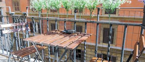 A balcony with a wooden table and chairs, surrounded by a metal railing.