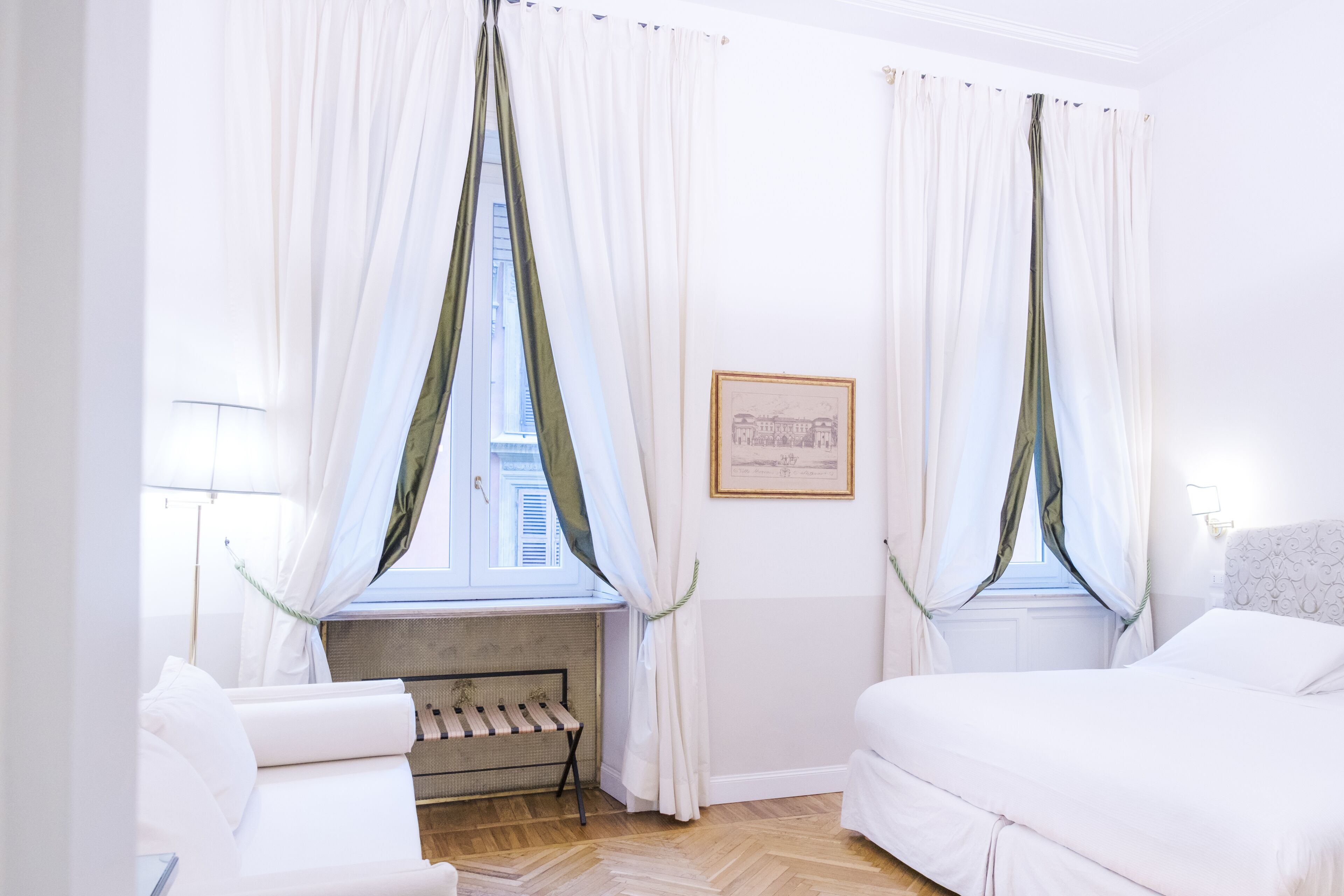 A hotel room with two beds, a bench, and a window with sheer curtains.
