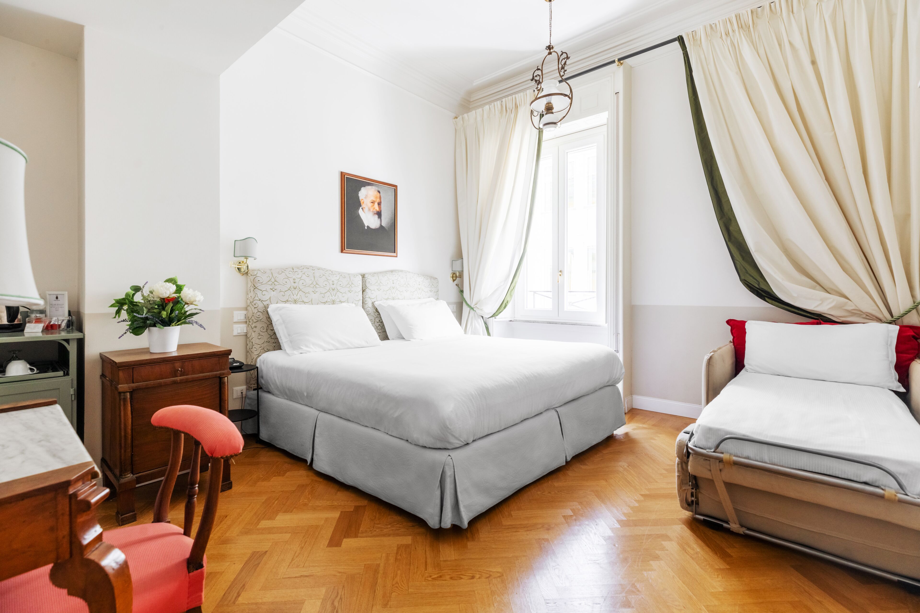 Un dormitorio con cama, una silla, un escritorio y una ventana con cortinas.