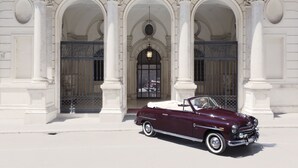 A classic maroon convertible parked in front of a grand building with ornate columns and a large arched entrance. - Relais Donna Lucrezia (Rome)