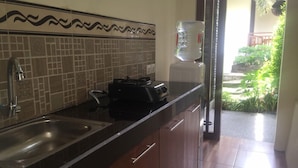 A kitchen with a tiled backsplash, a water dispenser, and a sink. - Pousada Canggu (Canggu)