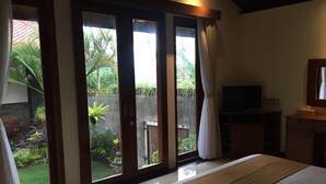 A bedroom with a large bed, a TV, and a view of a garden through sliding glass doors. - Pousada Canggu (Canggu)