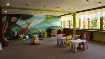 Une salle de jeux pour enfants avec une fresque murale, des meubles colorés et une fenêtre donnant sur des arbres.