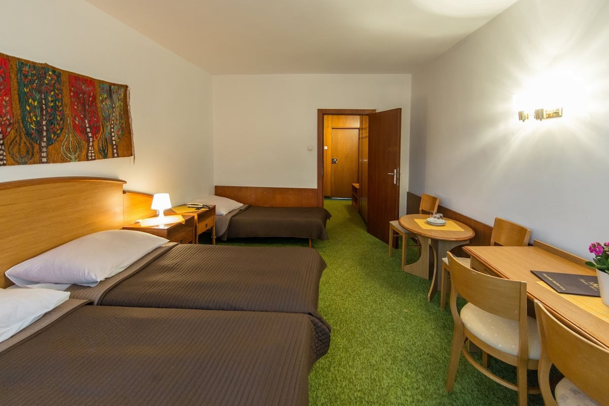 Een hotelkamer met twee bedden, een bureau, een stoel, een bijzettafeltje en een wandlamp.