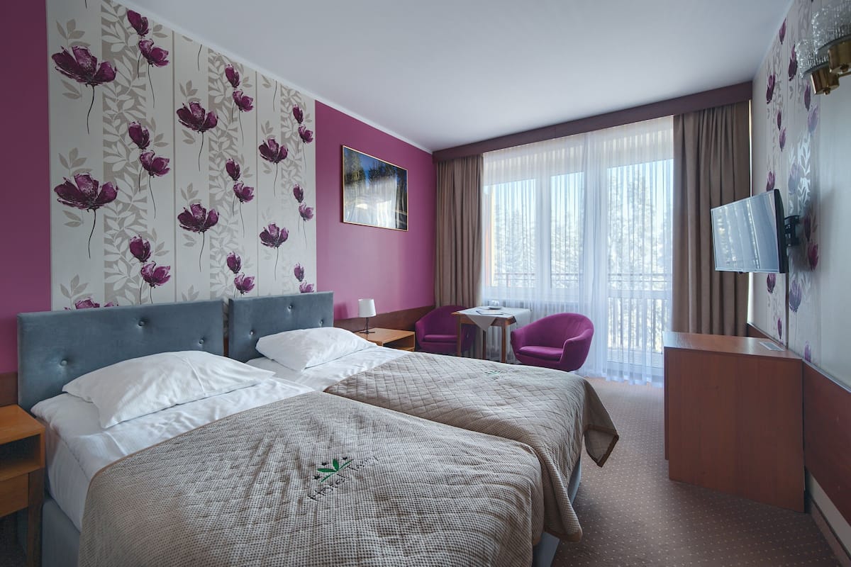Een hotelkamer met twee bedden, een bureau, een stoel, een televisie en een raam met gordijnen.