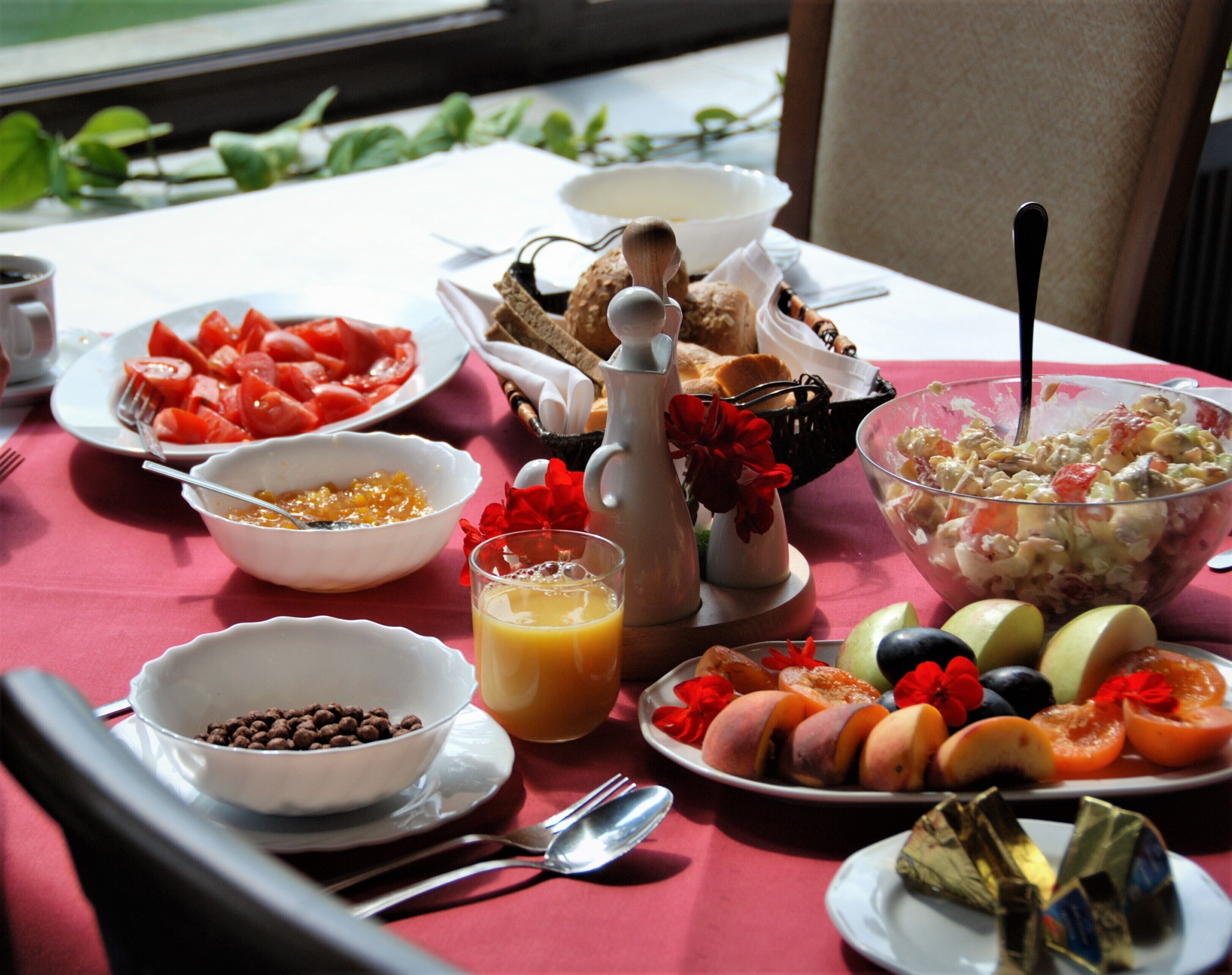 A breakfast table with various dishes including fruits, a bowl of cereal, and a glass of orange juice.