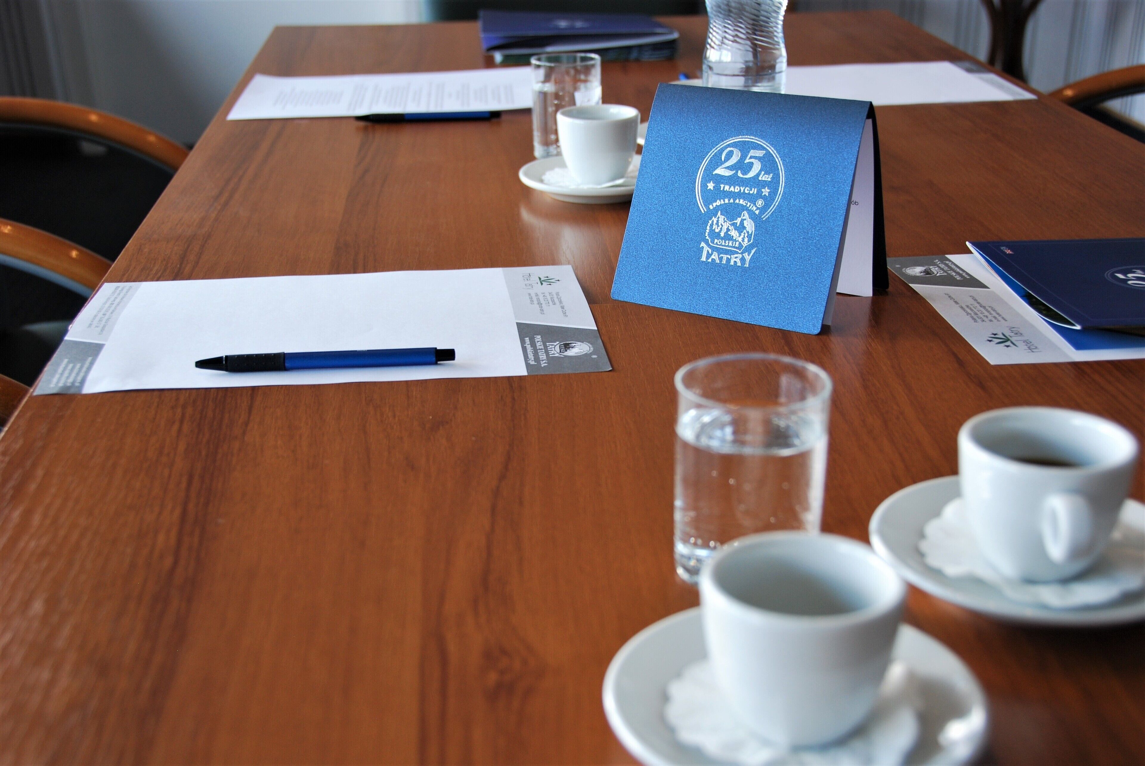 A wooden conference table with documents, a pen, a glass of water, and a coffee cup.