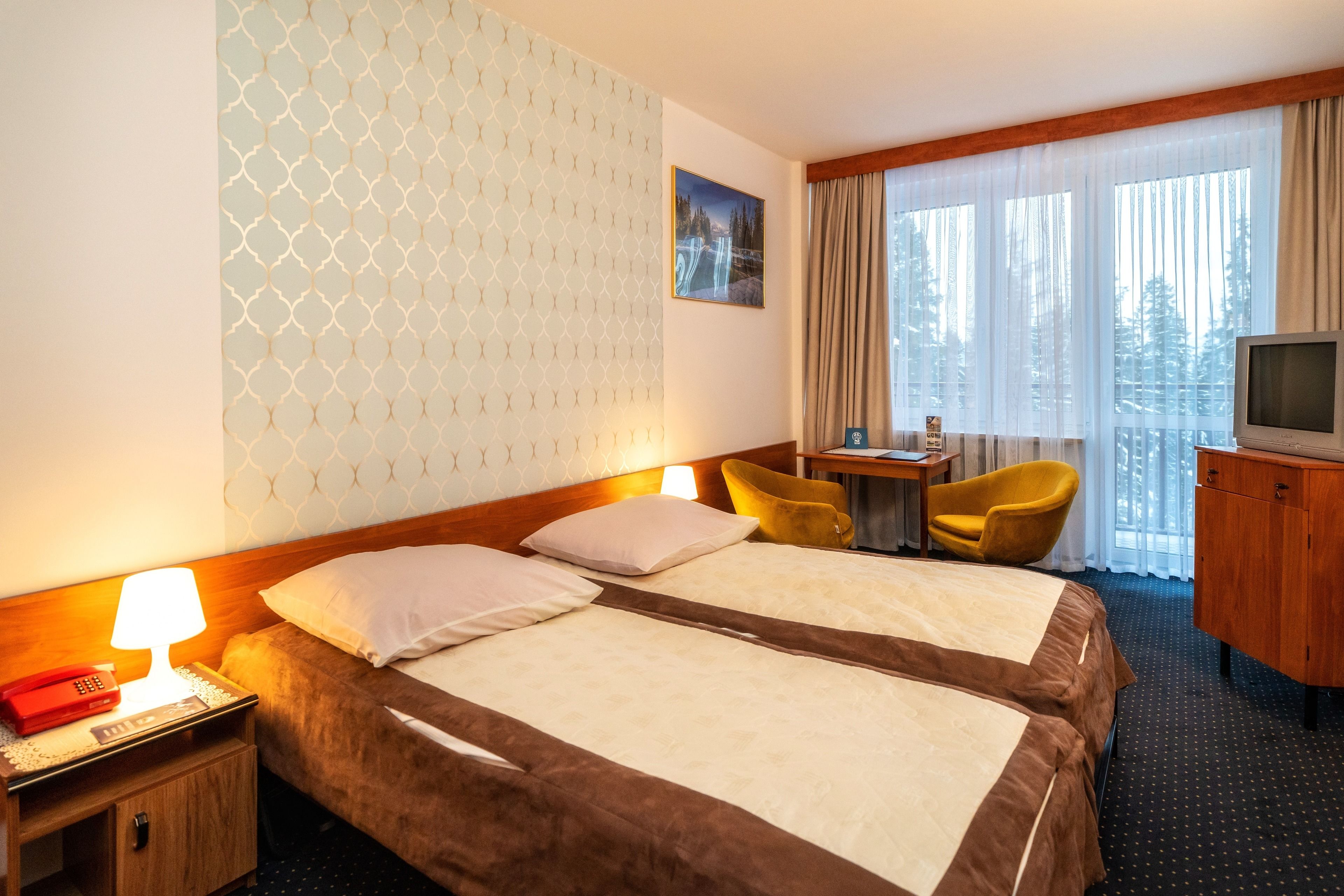 A hotel room with two beds, a desk with a chair, a television, and a window with curtains.