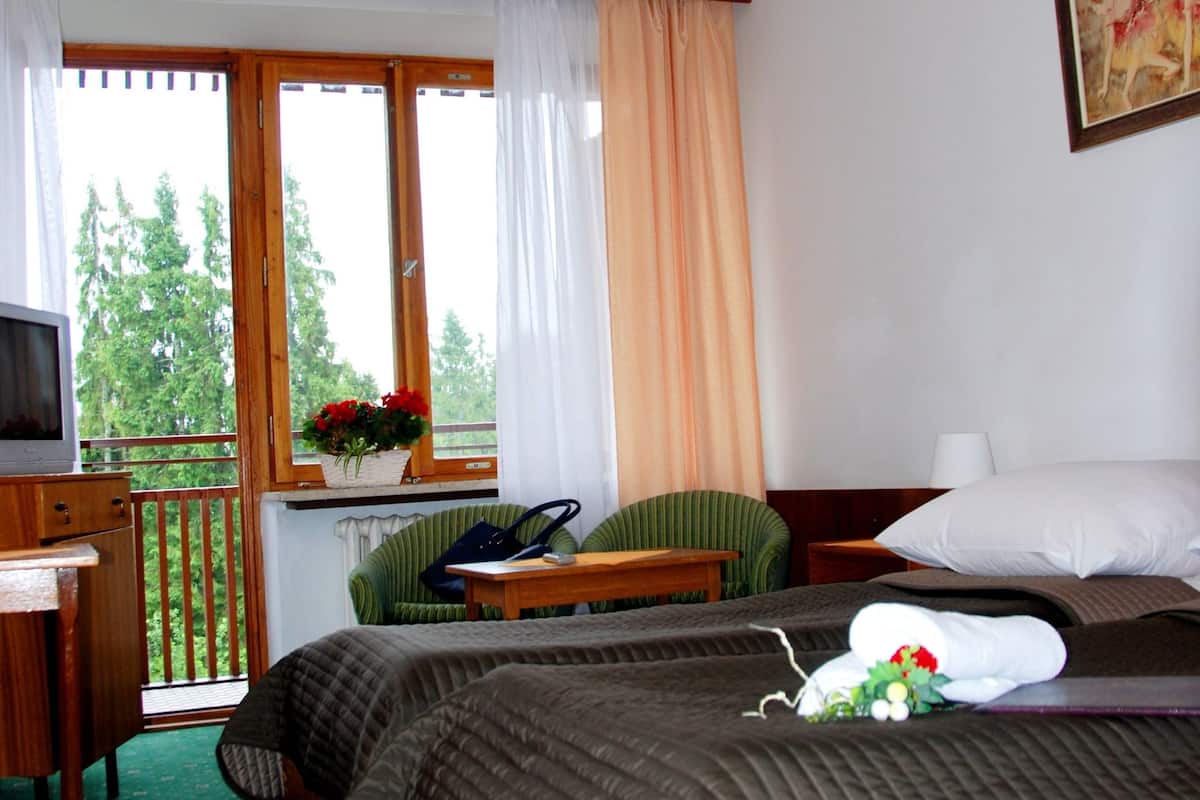Een hotelkamer met twee bedden, een bureau met televisie, een stoel, een raam met gordijnen en een schilderij aan de muur.