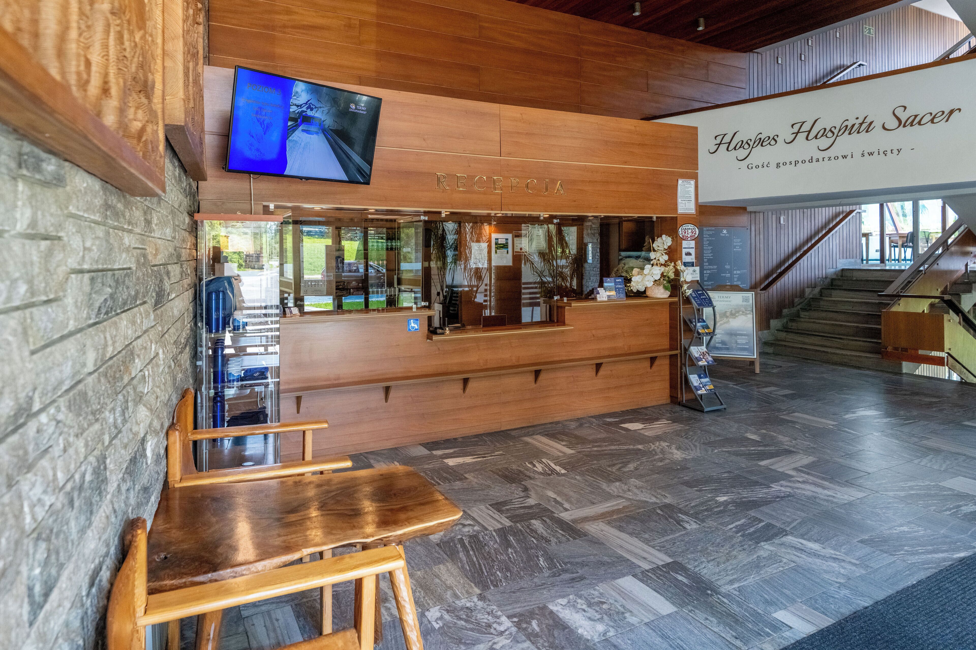 A reception area with a wooden counter, a television mounted above it, and a staircase leading upstairs.