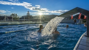 Une piscine avec de l’eau claire, une personne éclaboussant l’eau, et un bâtiment sur lequel on peut voir des banderoles Coca-Cola en arrière-plan.