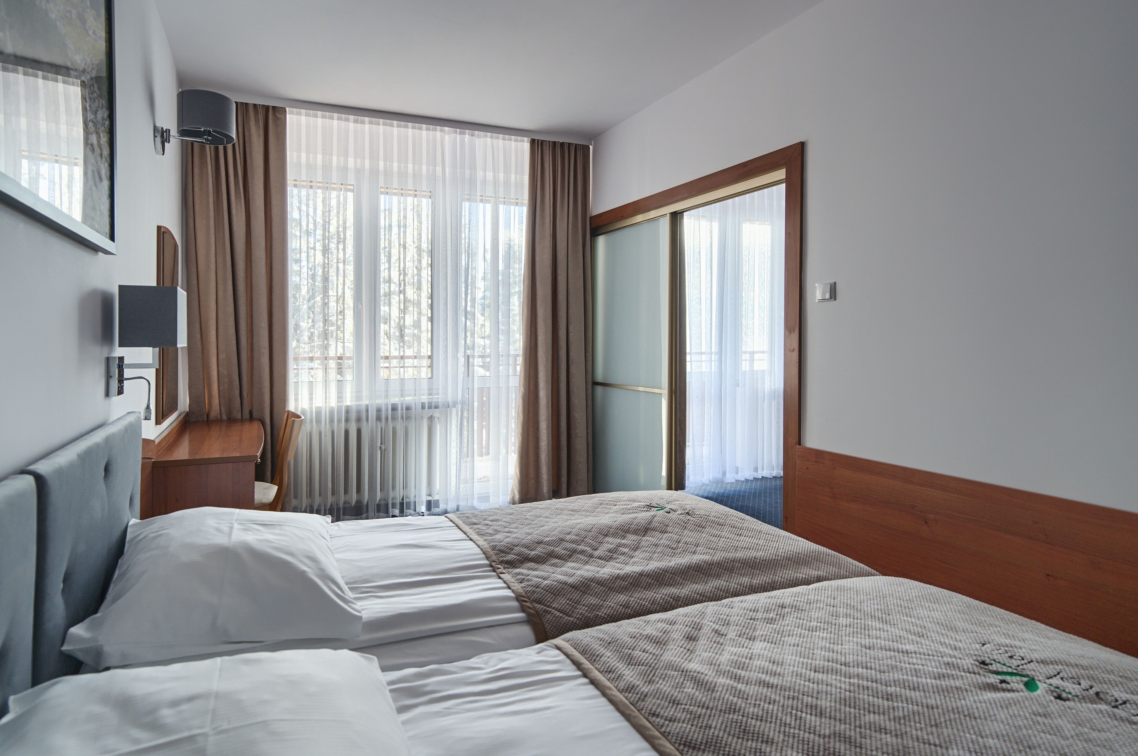 Habitación de hotel con dos camas, un escritorio y un ventanal grande con cortinas.