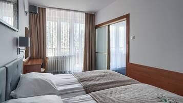 Habitación de hotel con dos camas, un escritorio y un ventanal grande con cortinas.
