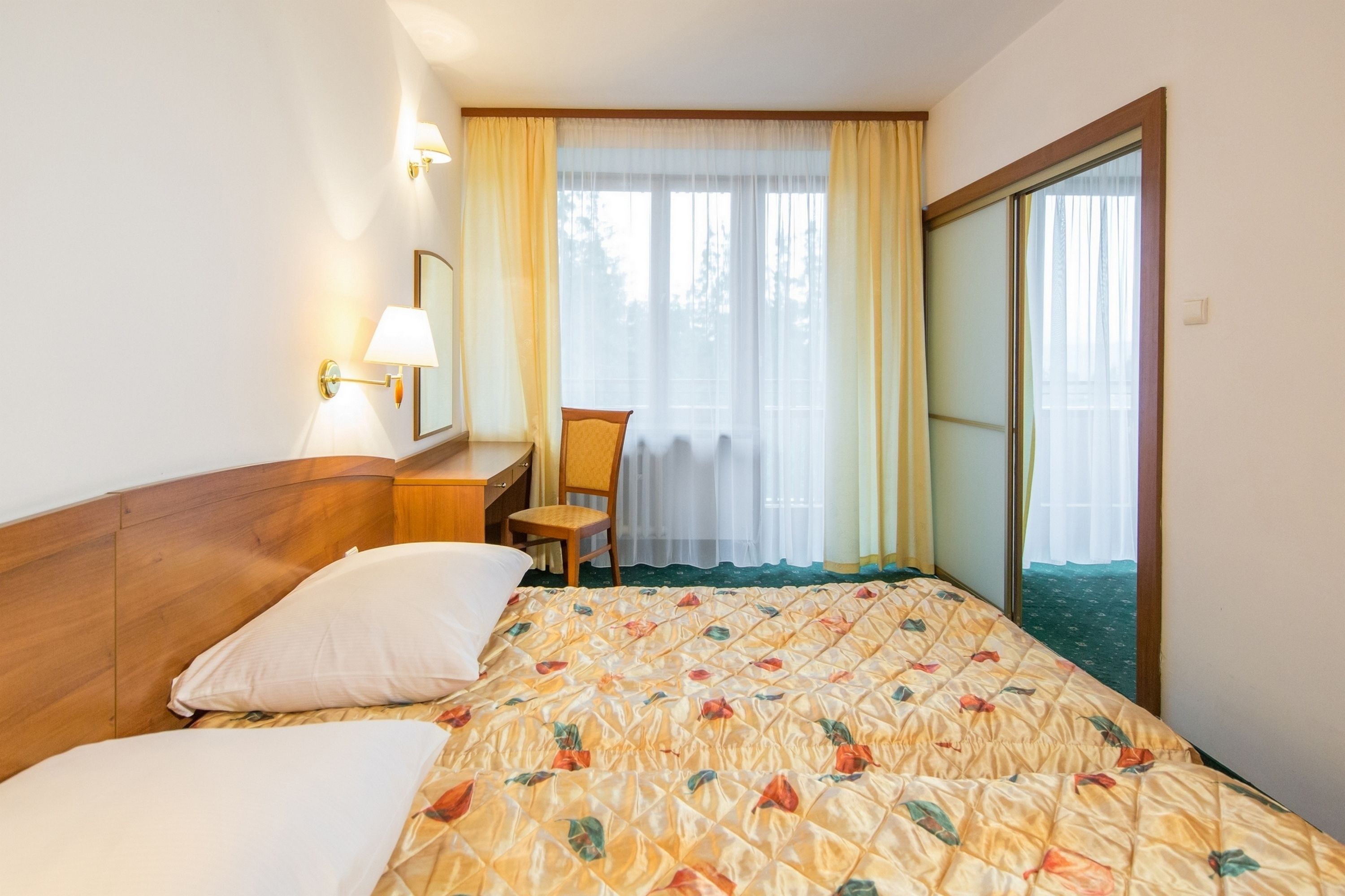 Una camera d'albergo con un letto, una scrivania, una sedia, una finestra con tende e vista sull'esterno.