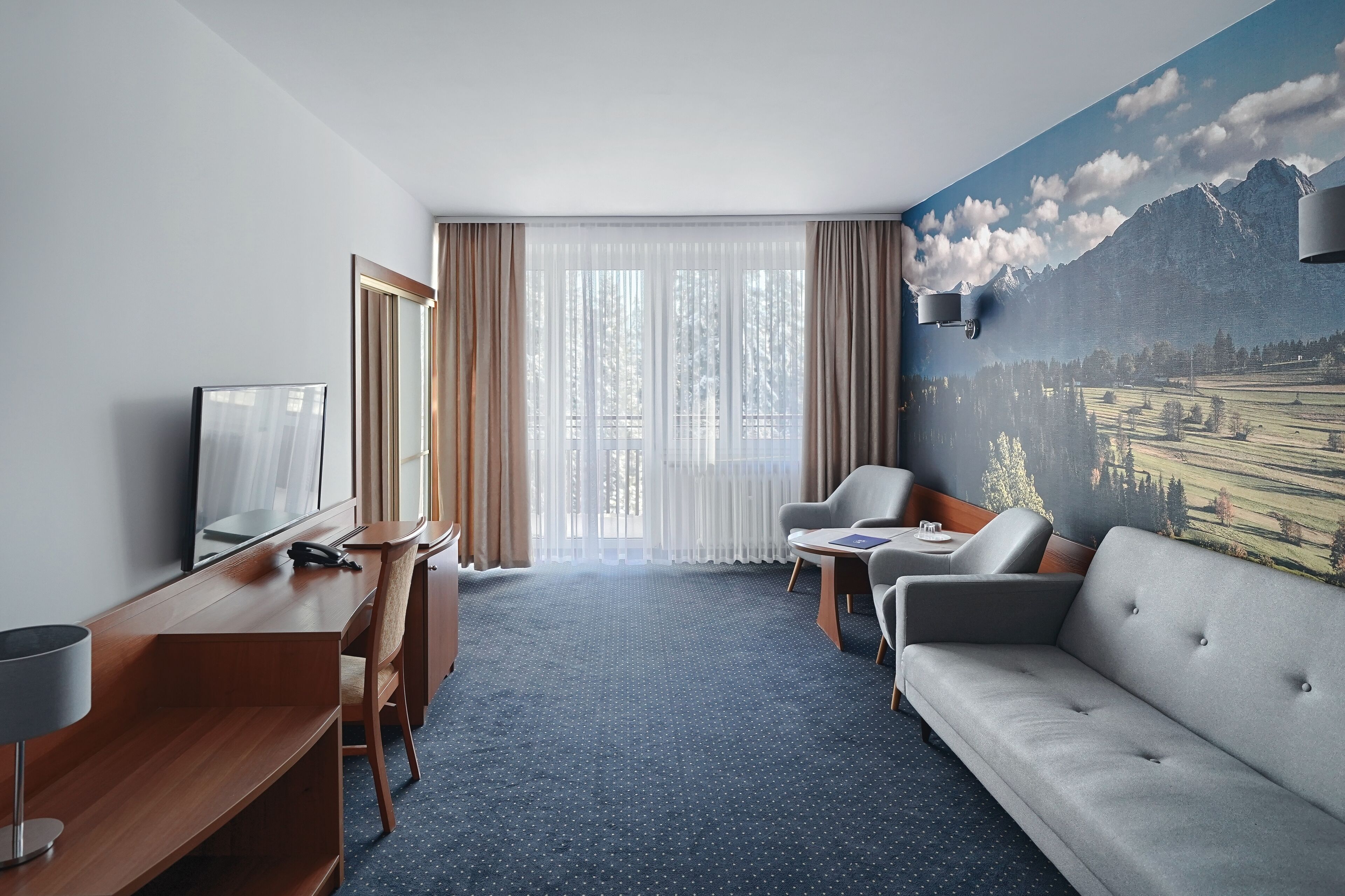 A hotel room with a large window, a sofa, a desk, and a TV.