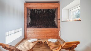Un sauna en bois comprenant deux chaises longues en bois, une grande fenêtre et un radiateur fixé au mur.