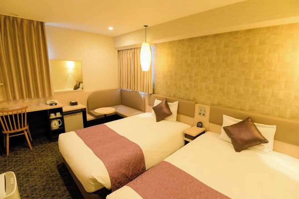 A hotel room with two beds, a desk, a chair, a small table, and a mirror.