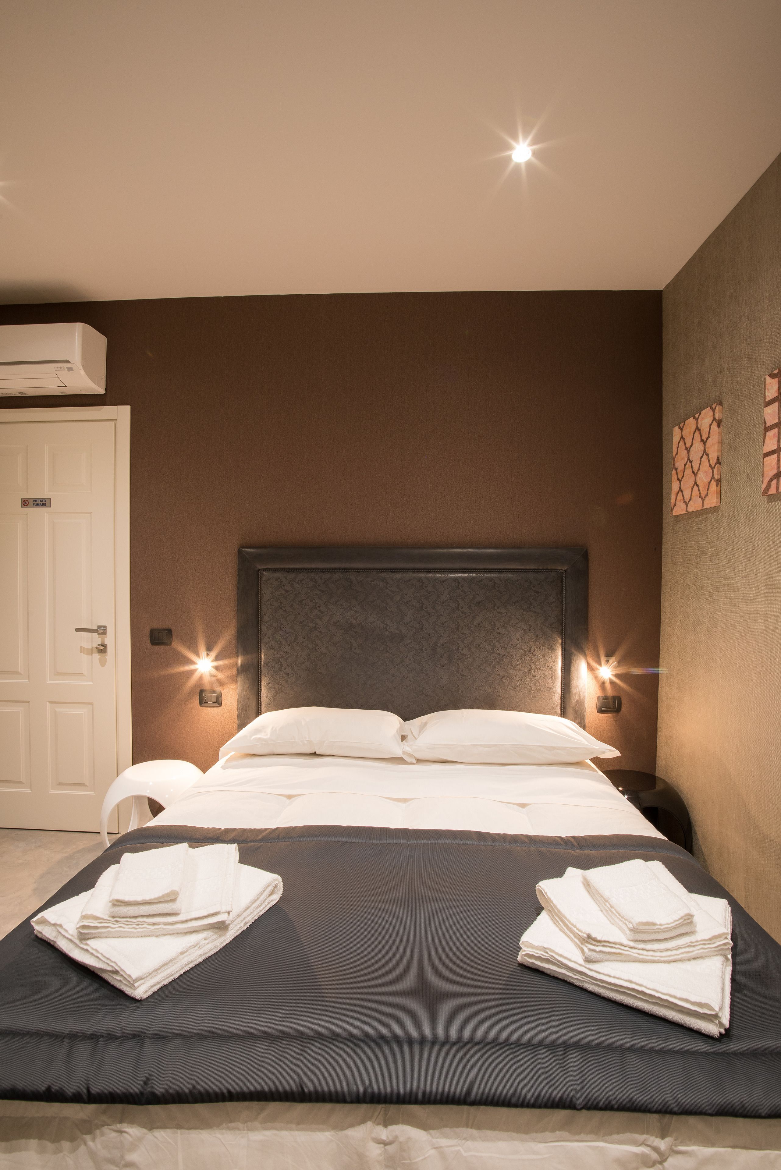 Cama bem arrumada com lençóis brancos, duas luminárias de cabeceira e ar-condicionado fixado na parede.