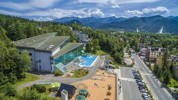 A hotel with a swimming pool, a parking lot, and a view of the surrounding mountains.