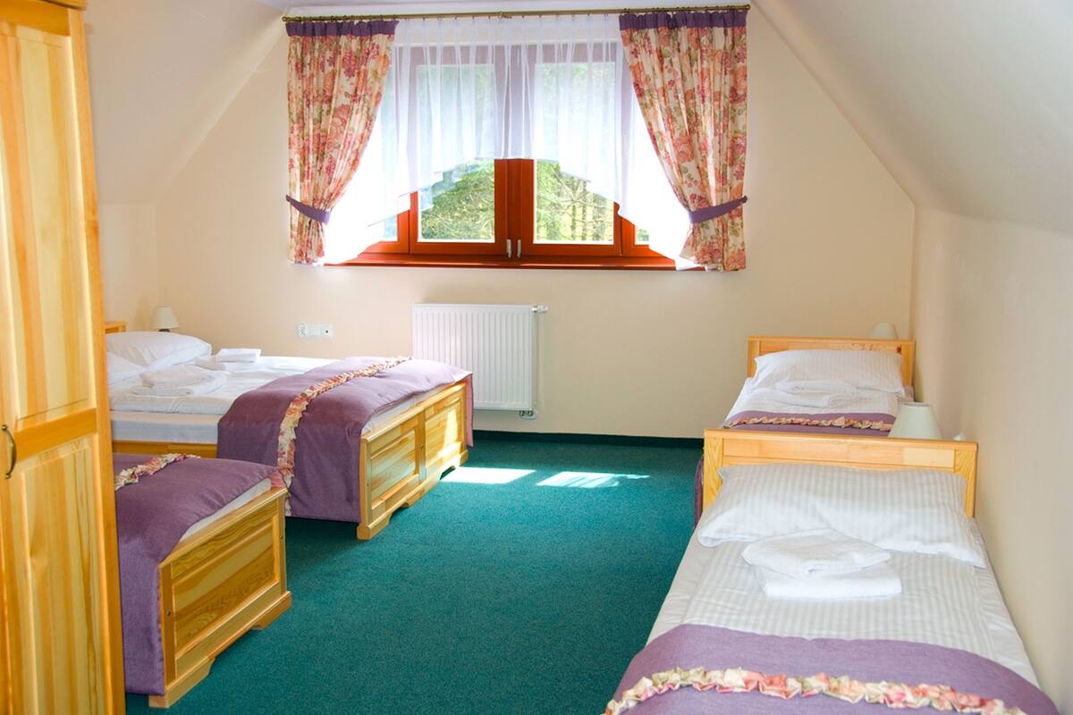 A bedroom with two single beds, a wooden wardrobe, a window with floral curtains, and a radiator.