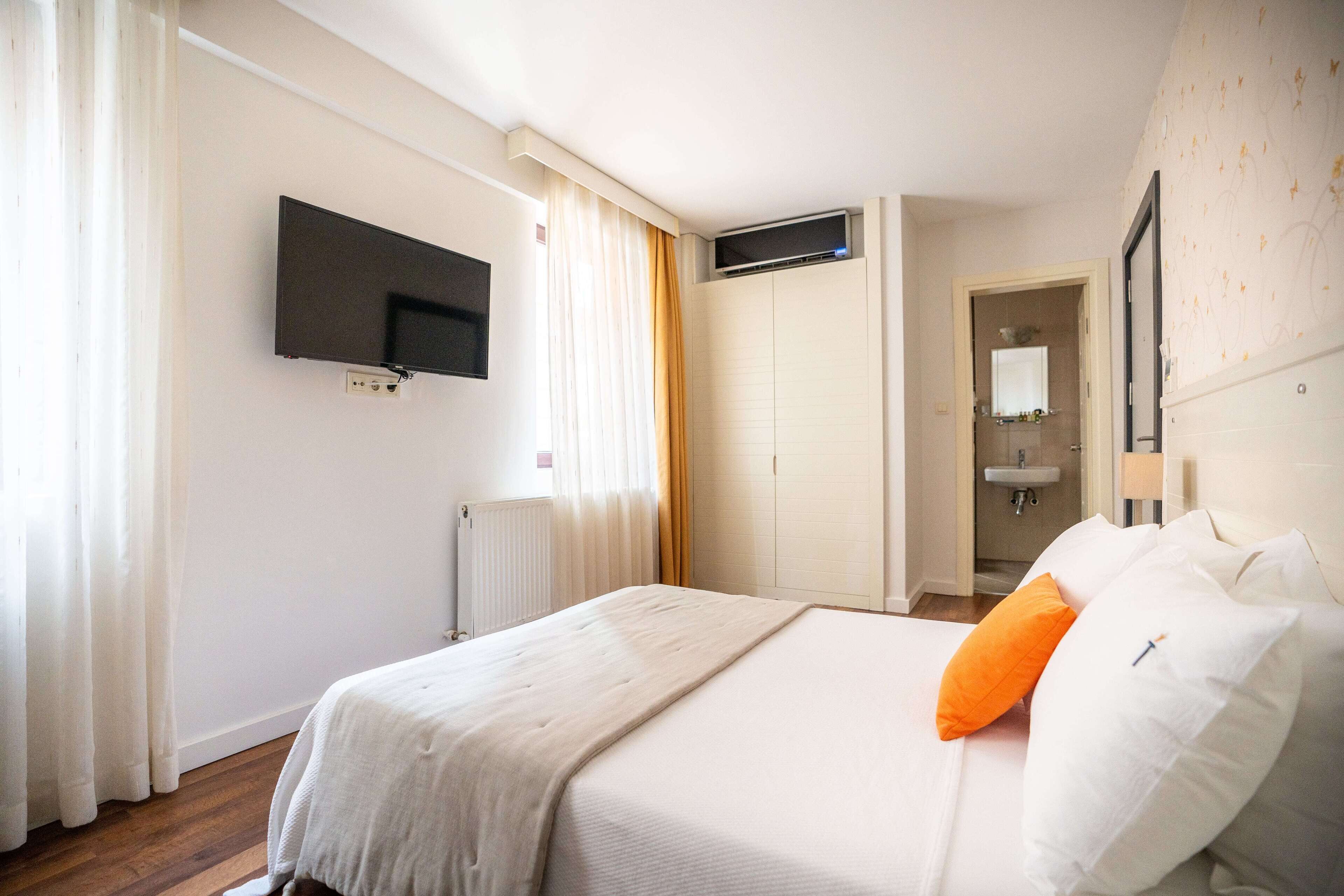 Habitación de hotel con cama, televisor montado en la pared, radiador y baño visible a través de una puerta abierta.