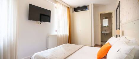Habitación de hotel con cama, televisor montado en la pared, radiador y baño visible a través de una puerta abierta.