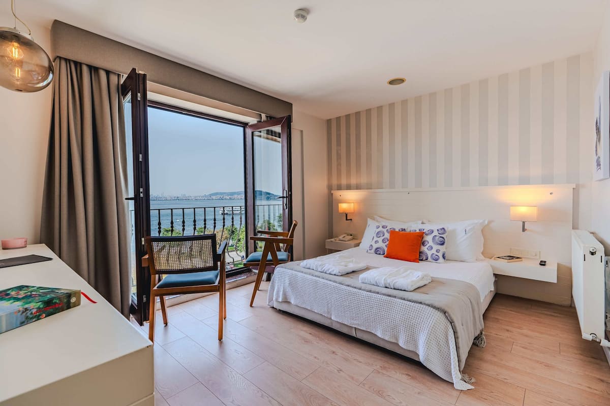 A hotel room with a large bed, a desk, a chair, and a balcony with a view of the city.