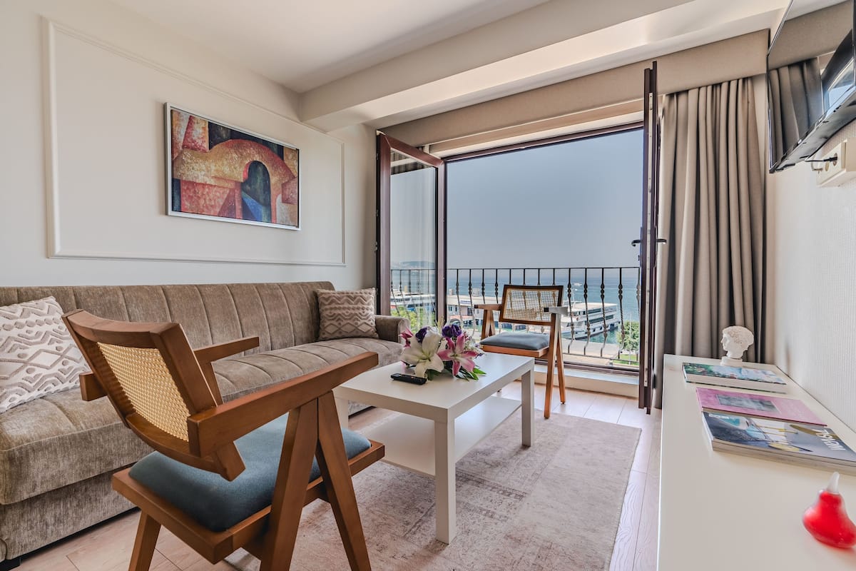 A modern living room with a sofa, a wooden chair, a coffee table, and a balcony with a view.