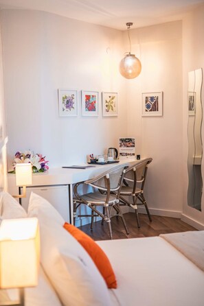 Ein modernes Hotelzimmer mit Bett, Schreibtisch und Stuhl. An der Wand hängen Bilder in Rahmen, eine Lampe und eine dekorative Vase mit Blumen.