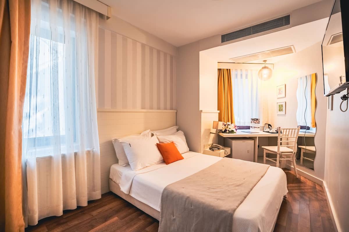A hotel room with a bed, a desk, a chair, and a mirror.