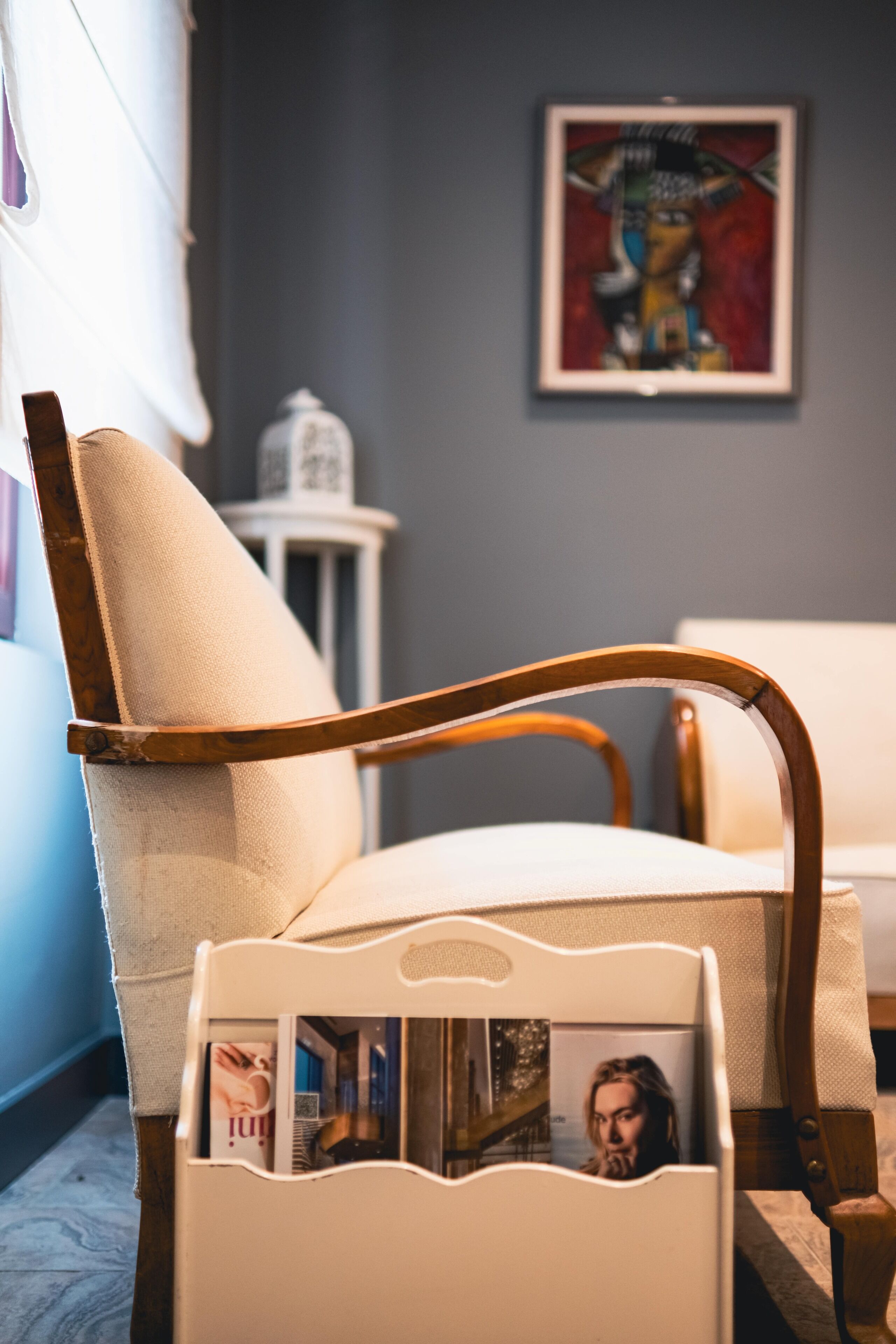 A chair with a magazine holder in a room with a gray wall and a framed artwork.