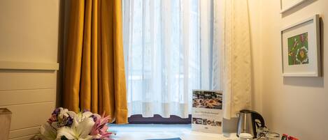 Habitación de hotel con una mesa dispuesta con un libro, una bandeja con tazas y una tetera, y un ramo de flores.