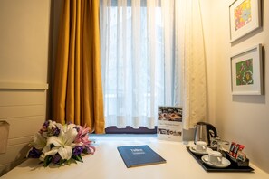 A hotel room with a window, a bouquet of flowers, a book, a tray with cups and a kettle, and framed pictures on the wall. - Tiara Buyukada (Adalar)