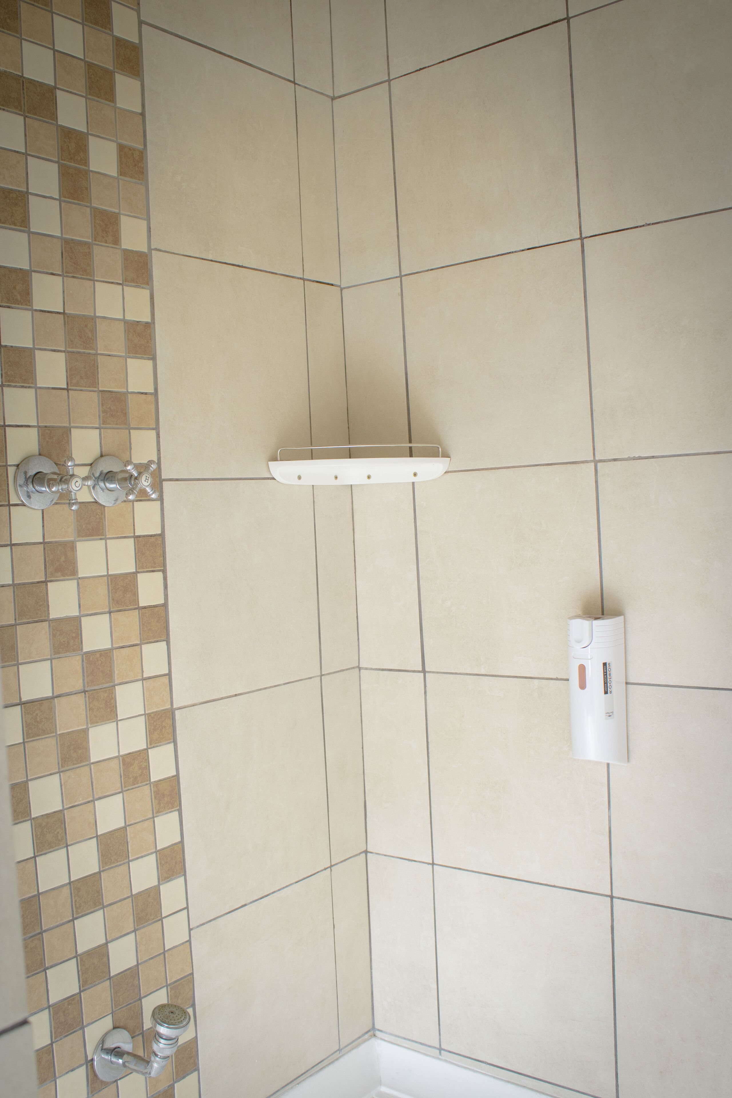 A tiled shower area with a white shelf and a wall-mounted light fixture.