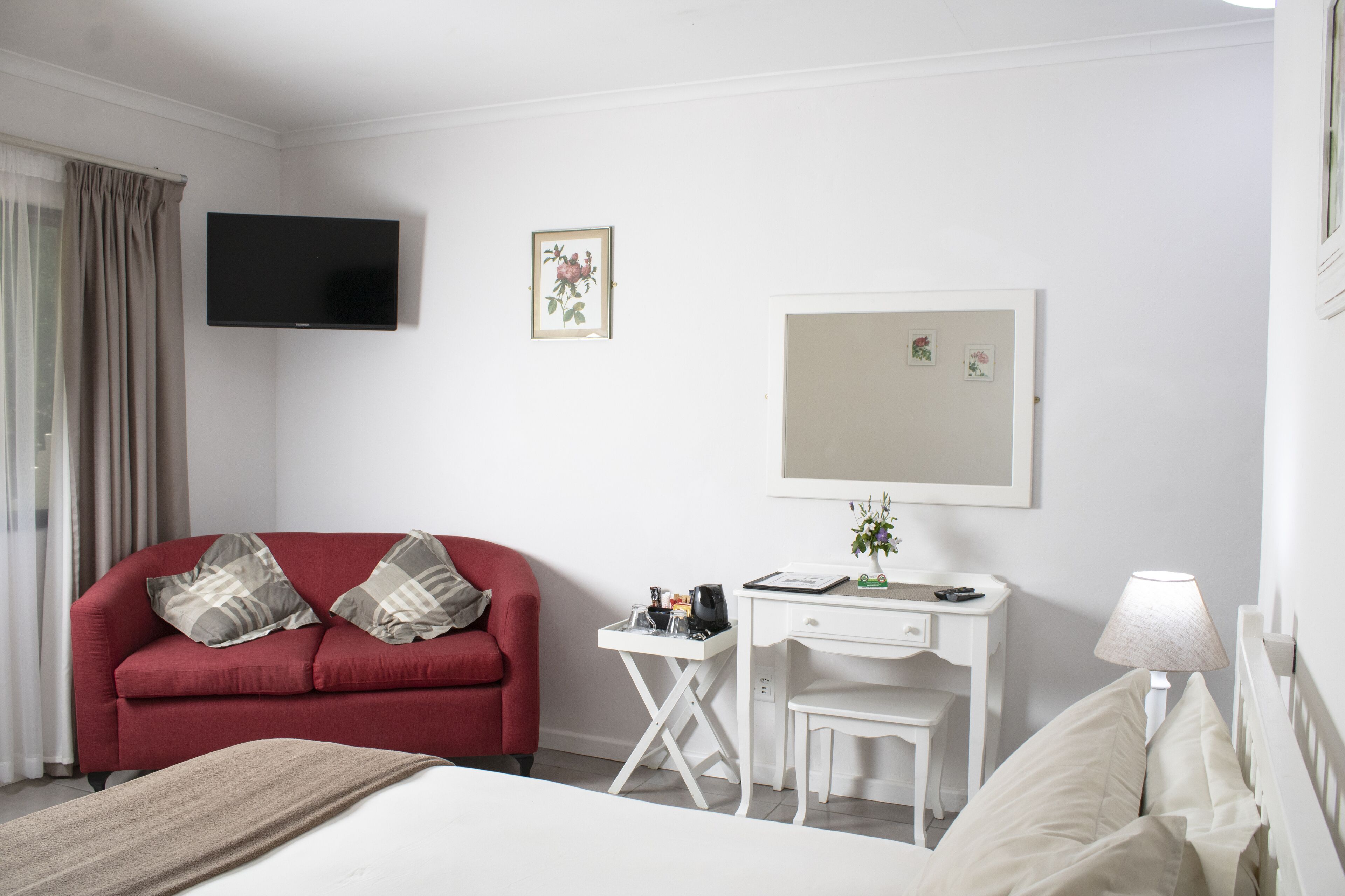 A hotel room with a red sofa, a white desk, a bed, a TV, and a lamp.