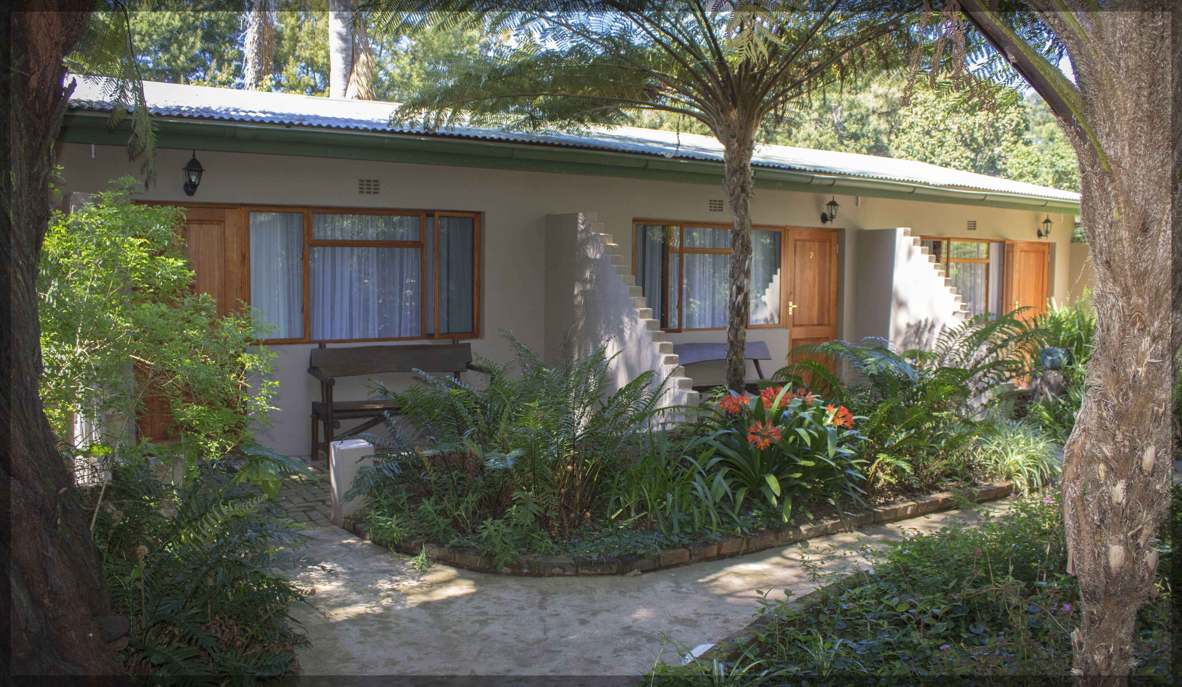 A single-story house with a front porch, a staircase leading to a second level, and a garden with various plants and flowers.