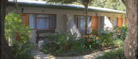A single-story house with a front porch, a staircase leading to a second level, and a garden with various plants and flowers.