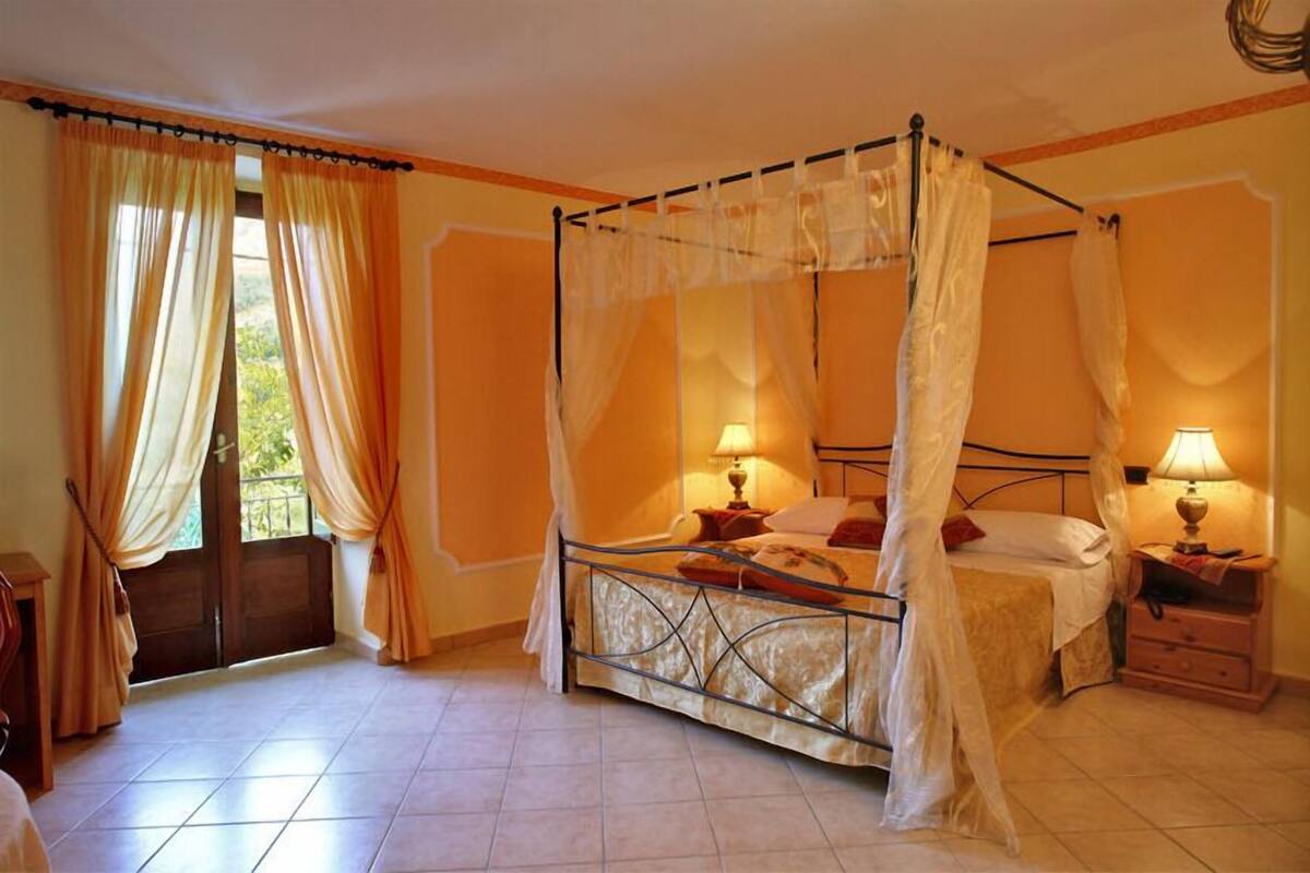 Una cama con dosel, dos mesitas de noche con lámparas, y vista al exterior a través de una puerta.