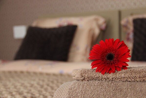 A bed with a red flower on the edge, a black pillow, and a beige blanket. - B&B at Room's (Ypres)
