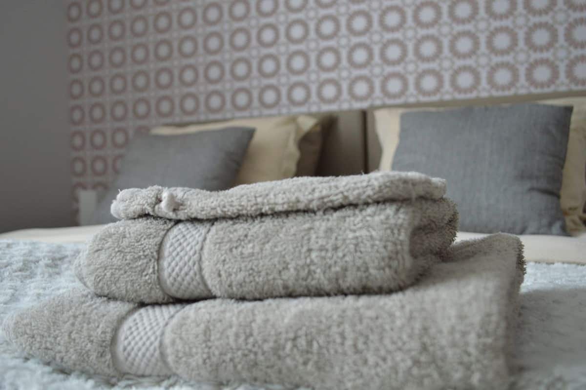 A neatly folded set of towels stacked on a bed with a patterned wall in the background.