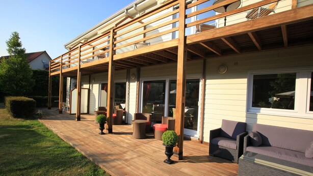 En overdækket terrasse med træbjælker, udendørs møbler og plantekasser.