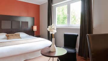 Een hotelkamer met een bed, een stoel, een tafeltje en een raam met gordijnen.