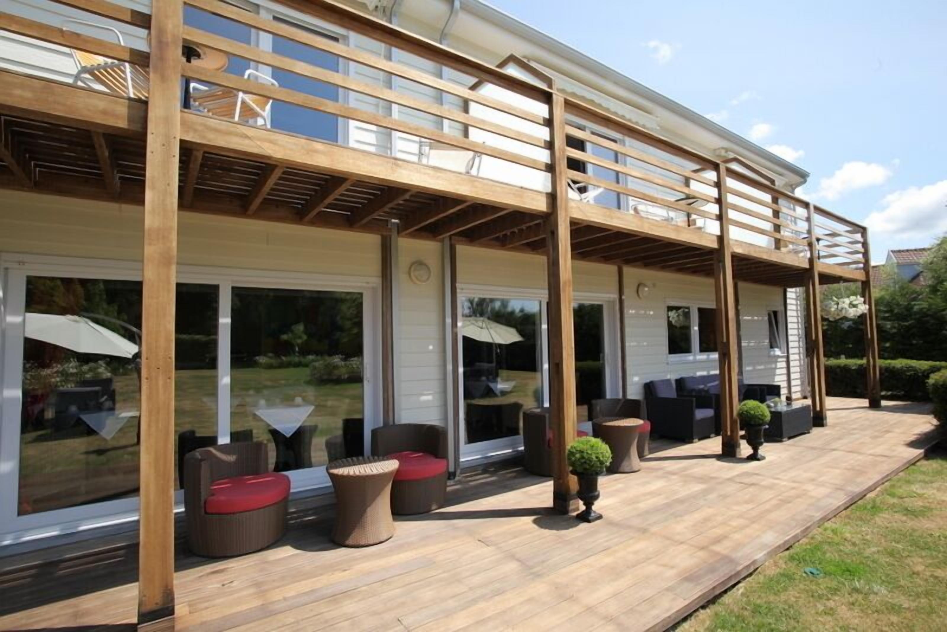 Un patio exterior techado con suelo de madera, asientos acolchados y plantas en macetas.