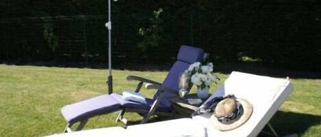 A sun lounger with a white umbrella, a vase with flowers, and a hat on the lounger.