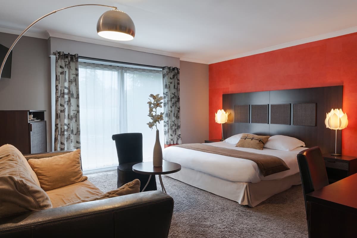 Habitació d'hotel amb un llit, una taula de treball, una cadira, una taula petita i una làmpada.