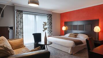 Una habitación de hotel con cama, escritorio, silla, una mesita y una lámpara.